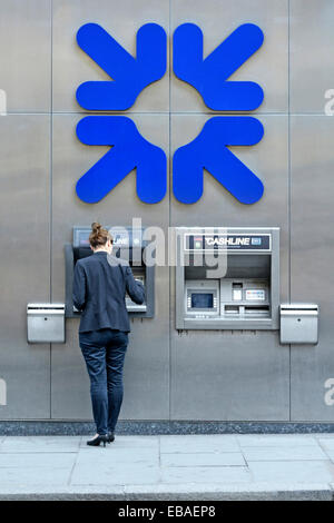 City of London woman using Royal Bank of Scotland cash dispenser with large sized company logo on wall above Stock Photo