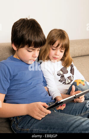 Children playing with a digital tablet on a sofa Stock Photo