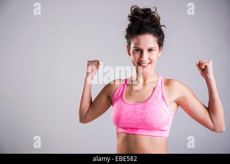 Close-up portrait of teenage girl exercising, smiling and looking at camera, studio shot on grey background Stock Photo