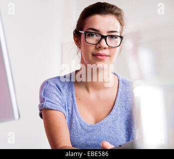Portrait of young woman in office, wearing horn-rimmed eyeglasses and looking at camera, Germany Stock Photo