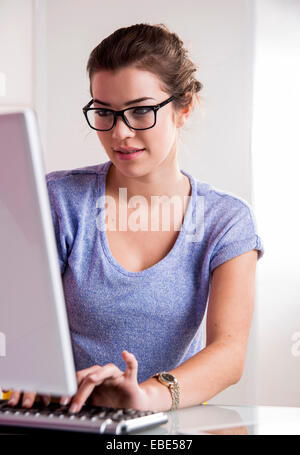 Young woman wearing horn-rimmed eyeglasses, working in office on desktop PC, Germany