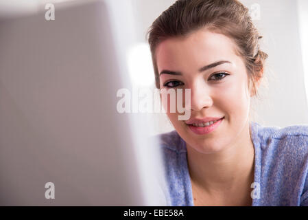 Close-up of young woman working in office on desktop PC, looking at camera and smiling, Germany Stock Photo