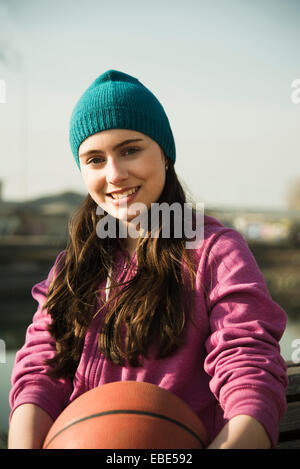 Close-up portrait of teenage girl outdoors, holding basketball and wearing toque, smiling and looking at camera, Germany Stock Photo