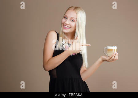 Happy Blond Woman Points Out to the Cup of Coffee Stock Photo