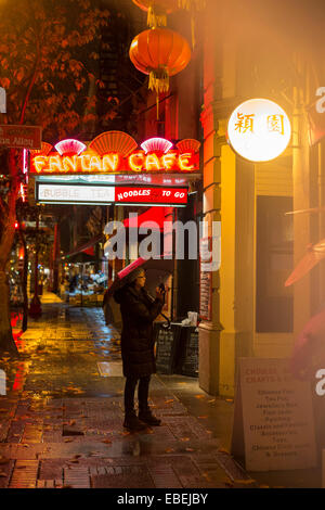 Chinese woman photographing Fan Tan alley entrance in Chinatown on rainy night-Victoria, British Columbia, Canada. Stock Photo