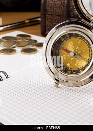 compass, gold coin and pen on checked notebook Stock Photo