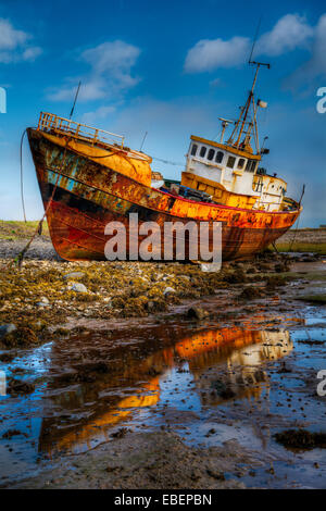 An approximate 30 meter Steel fishing boat sitting on the bottom during low tide on a bright cloudy blue sky day. Stock Photo