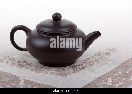 Traditional asian clay teapot isolated on beige handmade lace doily Stock Photo