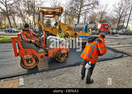 An asphalt spreader is used to place layer of asphalt and steam roller follows on a city Stock Photo