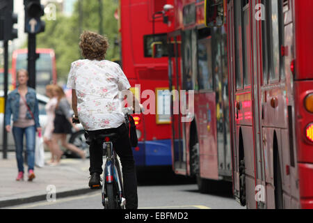 A female cyclist traveling next to a line of red London buses in Oxford Street. Stock Photo