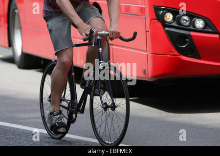 A cyclist and red London bus traveling along a road Stock Photo