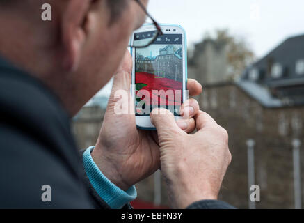Man using a mobile phone to take a photograph of the poppies at the Tower of London, England, UK Stock Photo