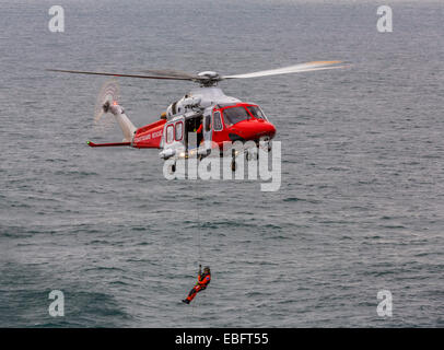 A view of an Augusta HM Coastguard Search and Rescue helicopter with the winchman lowered to the sea, the English channel, England UK Stock Photo