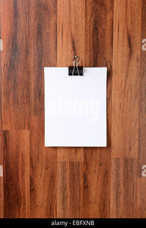 Blank sheets of paper held by a clip hanging from a nail in the middle of a dark wood wall. Vertical format. The blank white pap Stock Photo