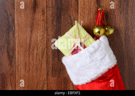 Closeup of a Christmas stocking filled with presents hanging from a hook on a wood wall. Two jingle bells hang from the hook als Stock Photo