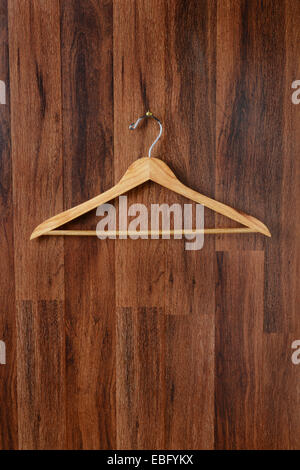 Closeup of an empty wooden hanger hanging from a hook on a dark wood paneled wall. Vertical format. Stock Photo