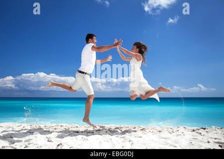 Happy newlyweds jumping up on beach with blue sky background Stock Photo