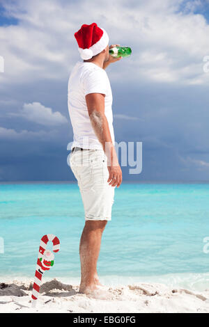 Man in Santa Helper hat looking to the sea and drinking champagne from a bottle. Celebration New Year Stock Photo