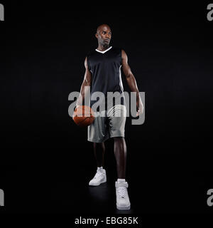 Full length portrait of young professional basketball player standing over black background. African young man in sportswear. Stock Photo