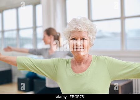 Two women doing stretching and aerobics workout at gym. Senior woman with her trainer in background during physical training. Stock Photo