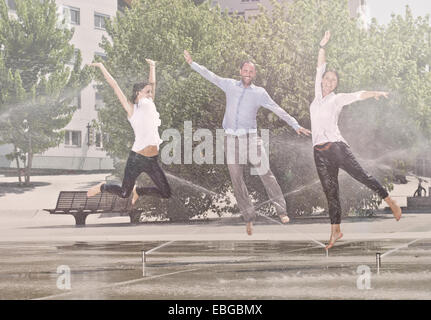 Two women and one man jumping in the park, between water sprinklers, Innsbruck, Tyrol, Austria Stock Photo