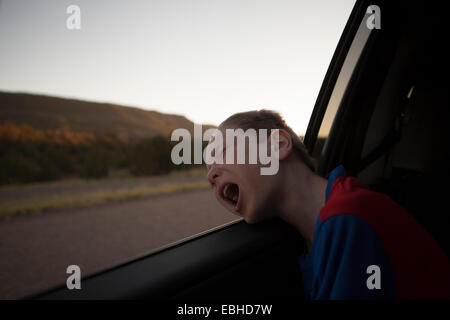 Boy leaning out of car window with eyes closed and mouth open