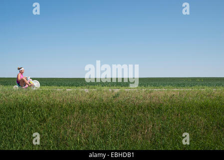 Teenage girl riding tricycle through field Stock Photo