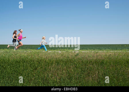 Three people running through field Stock Photo