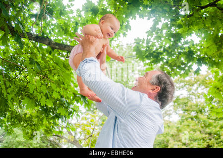 Grandfather lifting up baby granddaughter in park Stock Photo