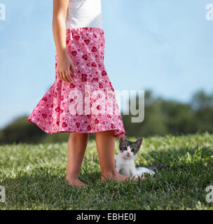 Young girl standing on grass with kitten, low section Stock Photo