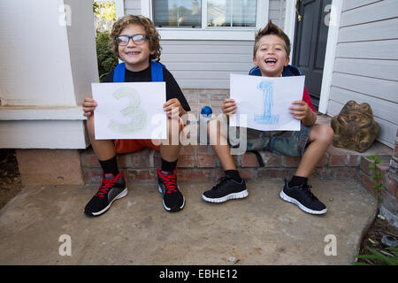 Portrait of two brothers sitting in porch holding up pieces of paper with 3 & 1 Stock Photo