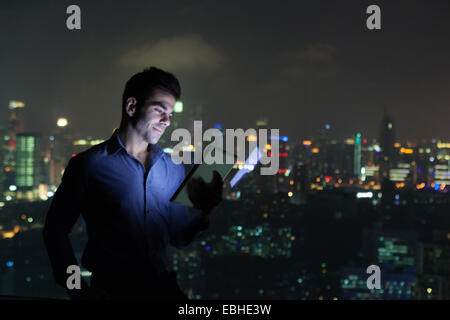 Young businessman looking at digital tablet in front of skyscraper office window at night, Shanghai, China