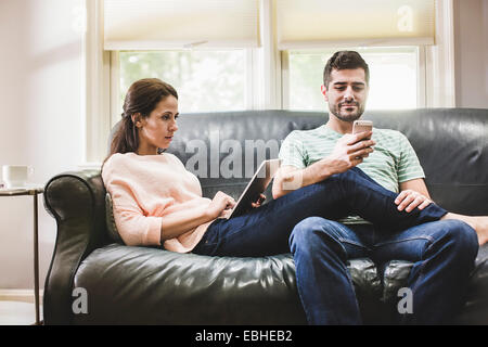 Couple using digital tablet and smartphone on sofa