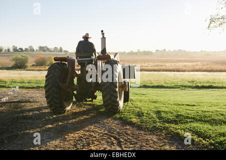 Rear view of senior male farmer driving tractor in field, Plattsburg, Missouri, USA