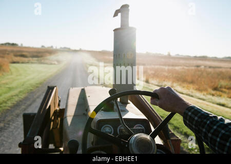 Over shoulder view of senior male farmer driving tractor on rural road, Plattsburg, Missouri, USA