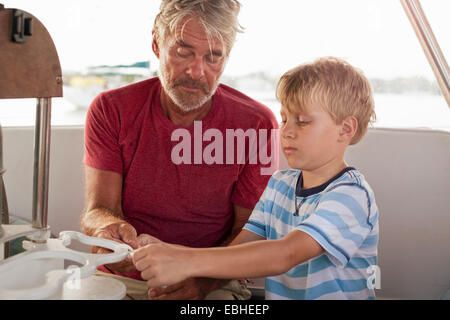 Grandfather teaching grandson to tie knots on sailboat Stock Photo