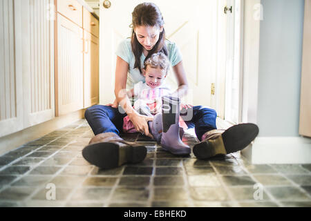 Mother and daughter putting on boots in kitchen