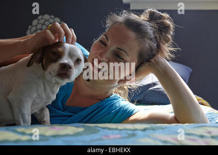 Woman lying on bed petting dog Stock Photo