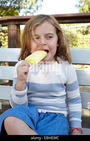Portrait of girl eating iced lolly on garden bench Stock Photo