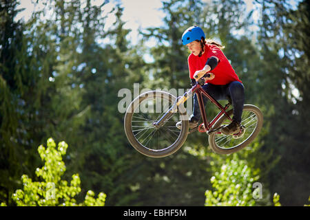 Young female bmx biker jumping mid air in forest