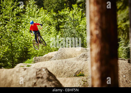 Young female bmx biker jumping mid air from rocks in forest Stock Photo