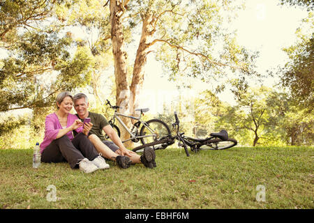 Mature cycling couple sitting in park looking at smartphone Stock Photo