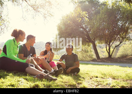 Four mature male and female runners sitting chatting in park Stock Photo