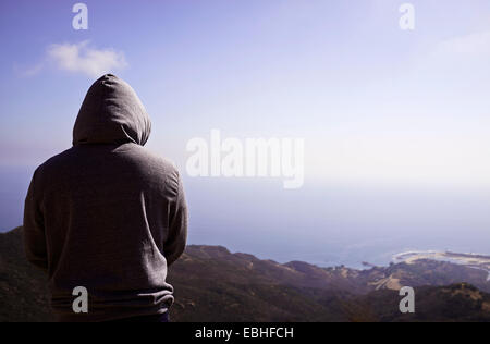 Rear view of mature man in hoody in front of coastline Stock Photo