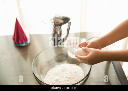 Hand holding egg over mixing bowl on table Stock Photo