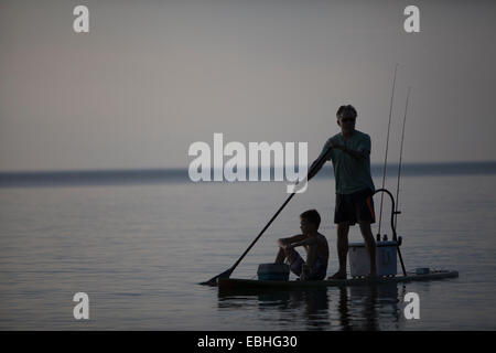 Silhouetted man and teenage son fishing from paddleboard in Lake Superior, Au Train Bay, Michigan, USA Stock Photo