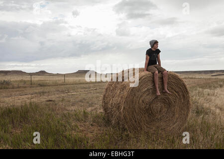 Teenage boy sitting on haystack in field, South Dakota, USA Stock Photo