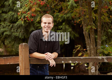Young man leaning against wooden fence in forest Stock Photo