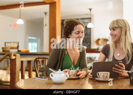 Two mid adult female friends looking at digital tablet in country store cafe Stock Photo