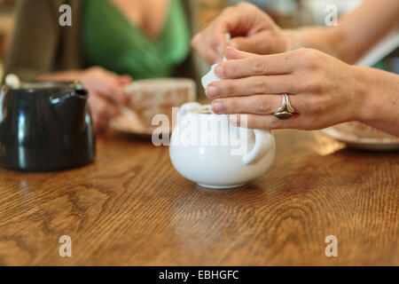 Cropped close up of two mid adult female hands picking sugar from bowl in country store cafe Stock Photo